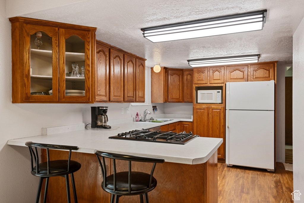 Kitchen featuring kitchen peninsula, white appliances, sink, light hardwood / wood-style flooring, and a kitchen bar
