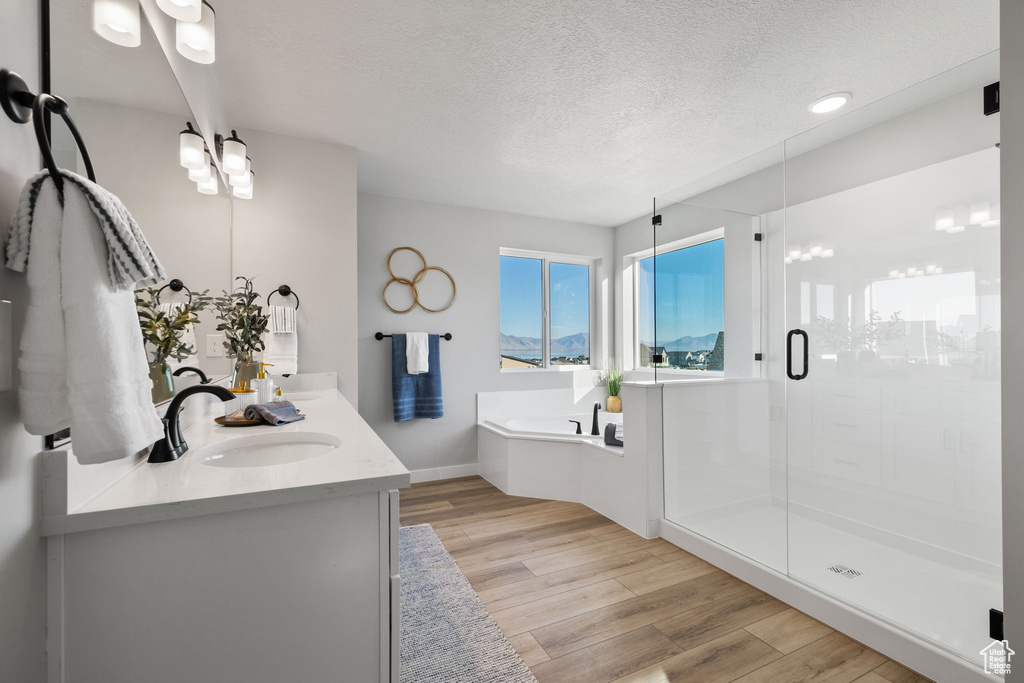 Bathroom with large vanity, a textured ceiling, hardwood / wood-style floors, dual sinks, and plus walk in shower