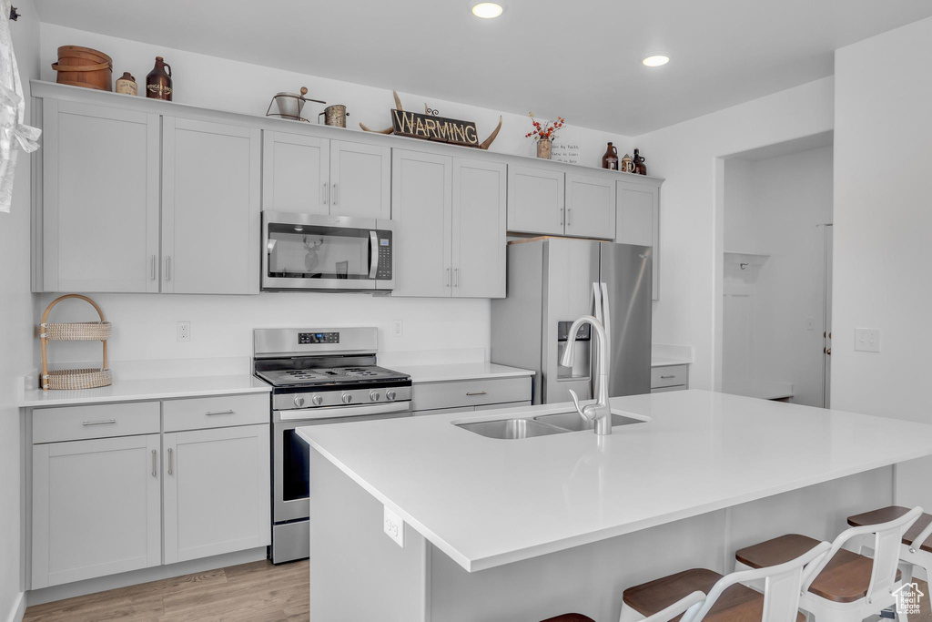 Kitchen featuring light hardwood / wood-style floors, stainless steel appliances, a kitchen bar, a center island with sink, and sink