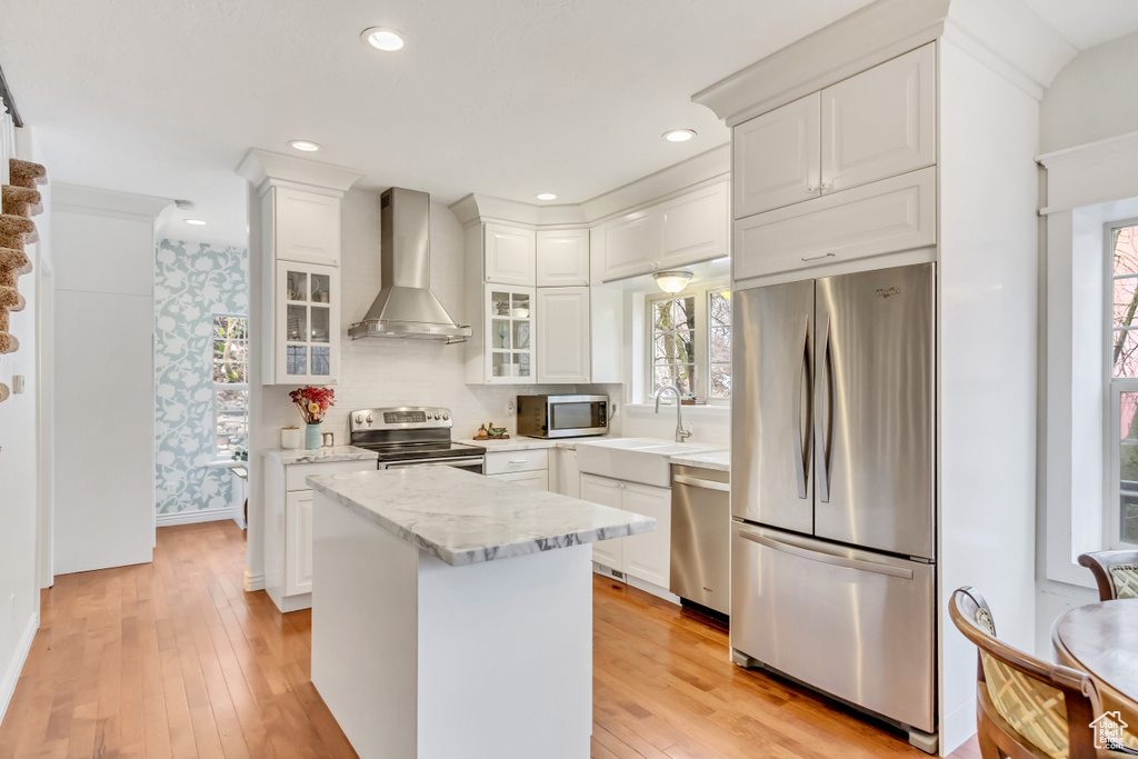 Kitchen featuring white cabinetry, light hardwood / wood-style flooring, stainless steel appliances, a center island, and wall chimney exhaust hood