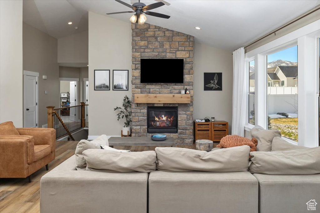 Living room with a stone fireplace, vaulted ceiling, light hardwood / wood-style flooring, and a wealth of natural light