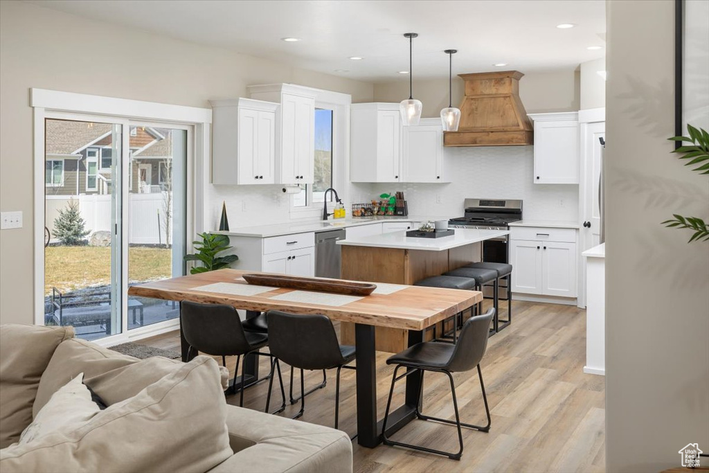 Kitchen with appliances with stainless steel finishes, custom exhaust hood, light hardwood / wood-style floors, white cabinets, and a kitchen island