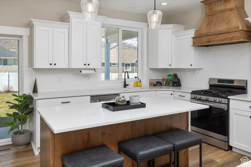 Kitchen featuring pendant lighting, premium range hood, appliances with stainless steel finishes, white cabinetry, and backsplash
