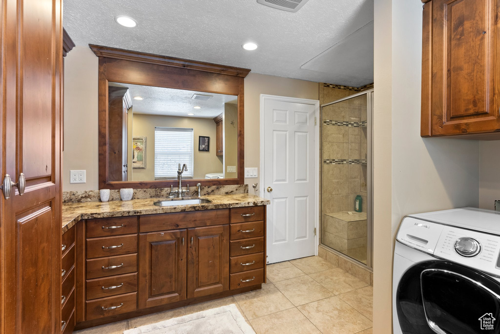 Laundry area featuring light tile floors, washer / clothes dryer, a textured ceiling, and sink