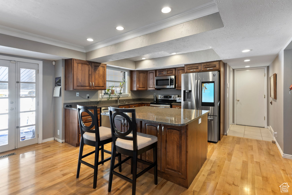 Kitchen with a kitchen bar, a textured ceiling, french doors, appliances with stainless steel finishes, and light wood-type flooring