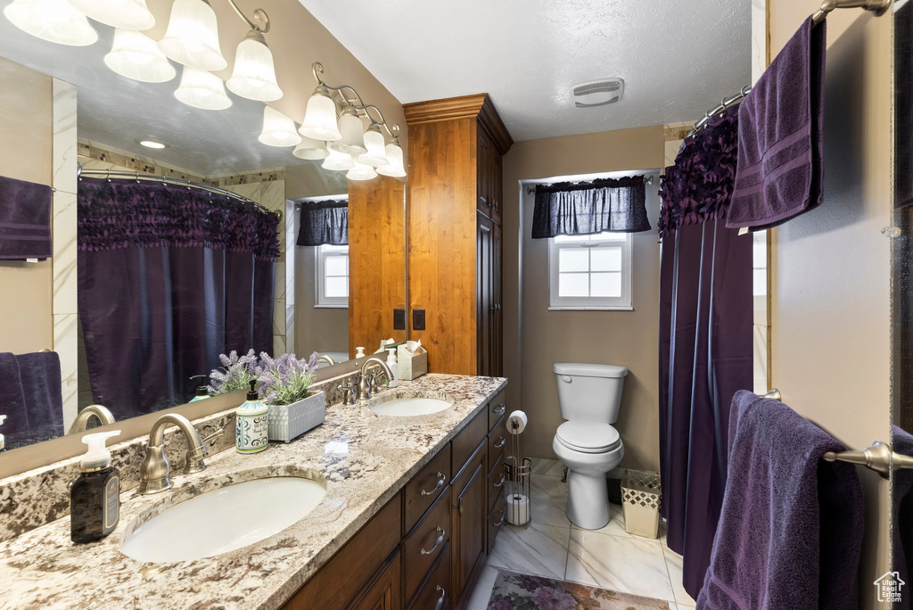 Bathroom featuring toilet, vanity with extensive cabinet space, tile flooring, and dual sinks