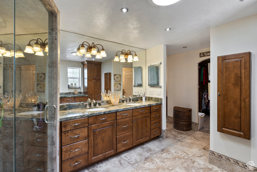 Bathroom featuring a shower with door, dual sinks, vanity with extensive cabinet space, and tile flooring