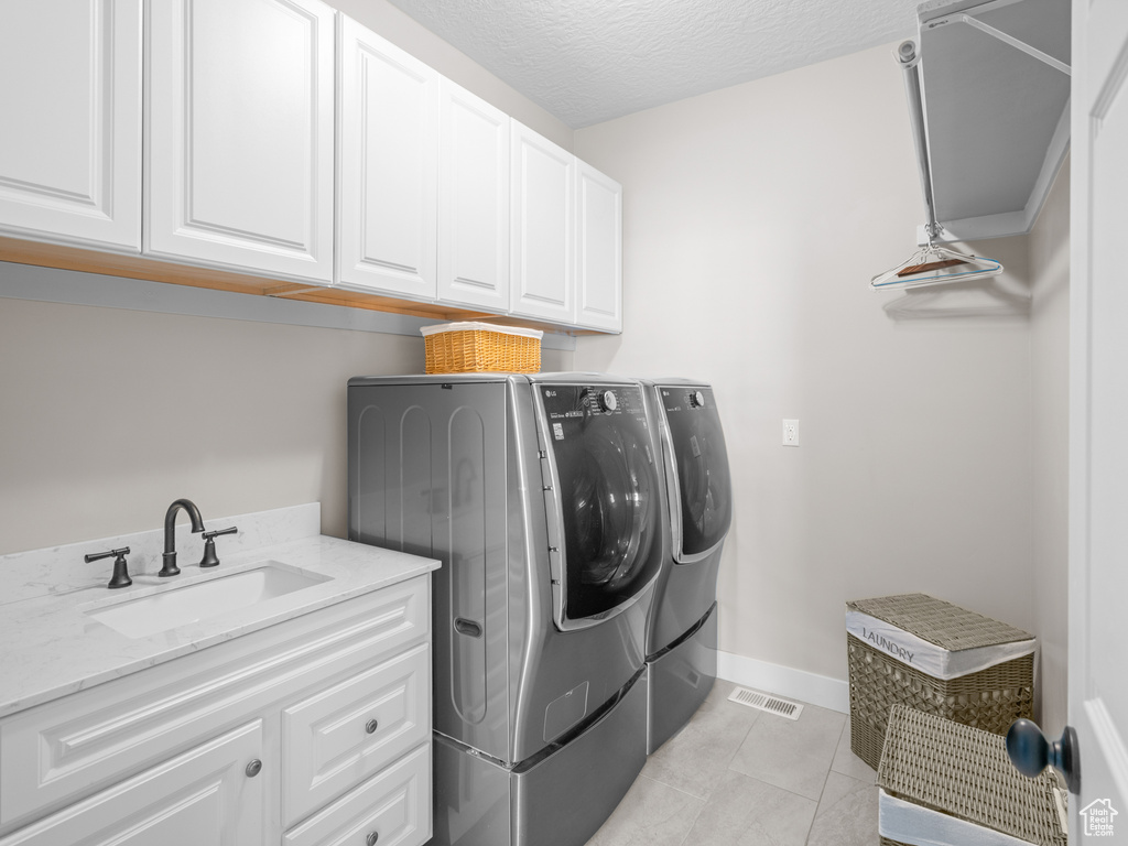 Clothes washing area with washing machine and clothes dryer, sink, light tile floors, cabinets, and a textured ceiling