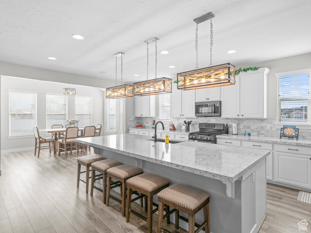Kitchen featuring pendant lighting, white cabinetry, appliances with stainless steel finishes, sink, and a center island with sink