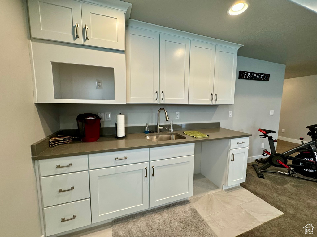 Kitchen featuring light colored carpet, white cabinetry, and sink
