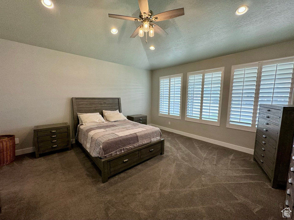Carpeted bedroom featuring a textured ceiling, multiple windows, ceiling fan, and vaulted ceiling