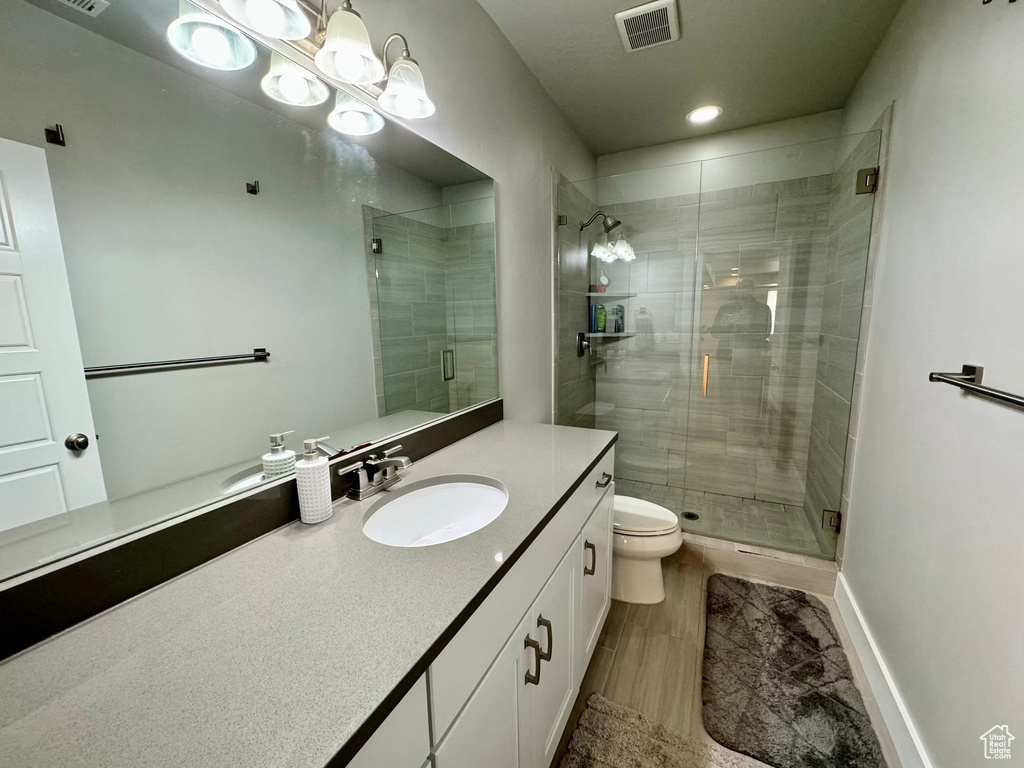 Bathroom with an inviting chandelier, vanity, toilet, and walk in shower
