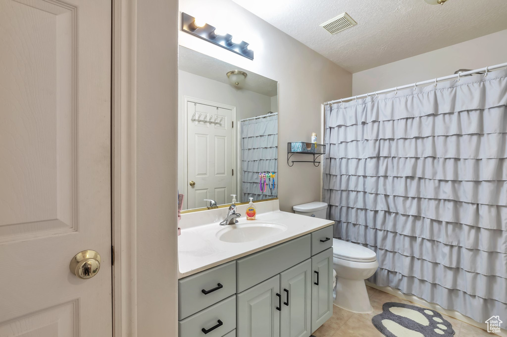 Bathroom featuring toilet, a textured ceiling, vanity with extensive cabinet space, and tile flooring