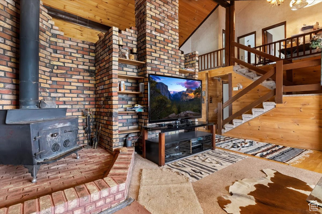 Living room featuring brick wall, high vaulted ceiling, wooden ceiling, and a wood stove