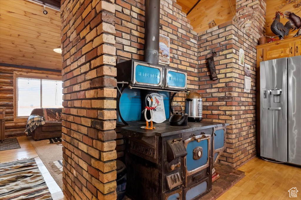 Kitchen featuring stainless steel fridge with ice dispenser, brick wall, light hardwood / wood-style floors, and a wood stove