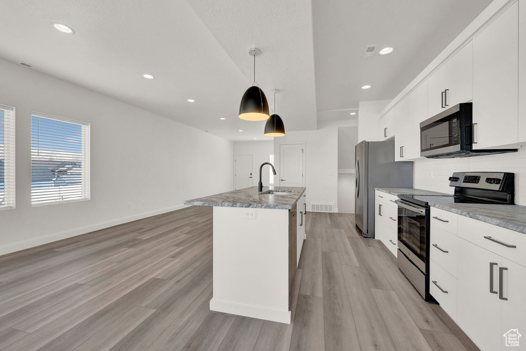 Kitchen featuring white cabinets, light wood-type flooring, a kitchen island with sink, and appliances with stainless steel finishes