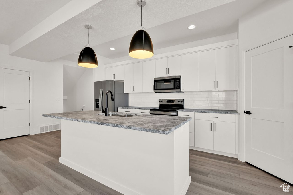 Kitchen with white cabinets, light hardwood / wood-style flooring, stainless steel appliances, and decorative light fixtures