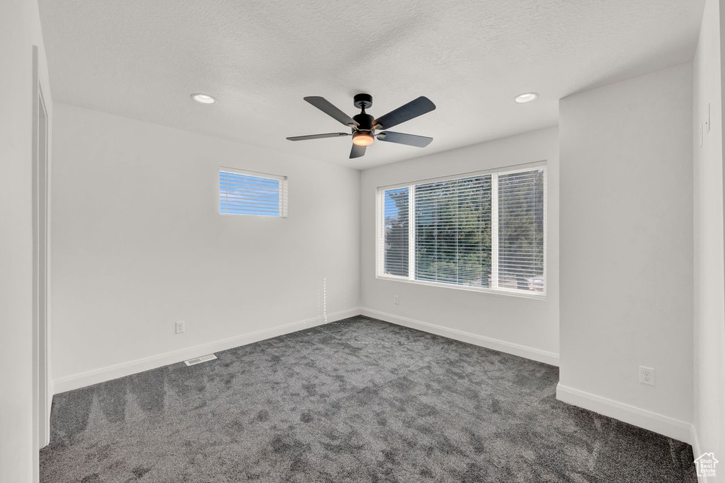Empty room with dark carpet, ceiling fan, and a healthy amount of sunlight