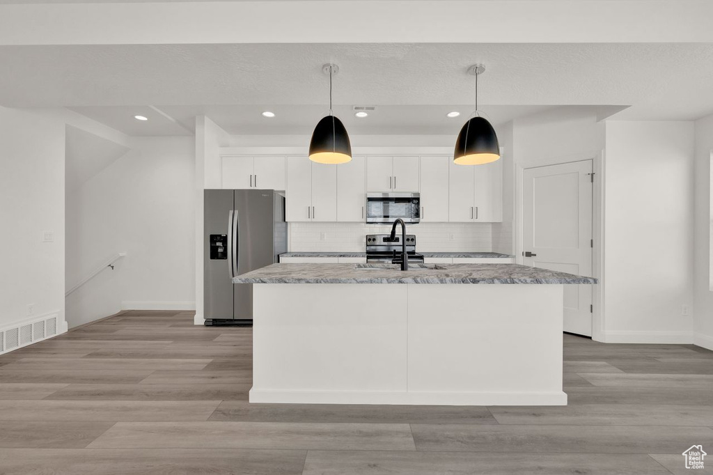 Kitchen with stainless steel appliances, white cabinets, a kitchen island with sink, and light hardwood / wood-style flooring