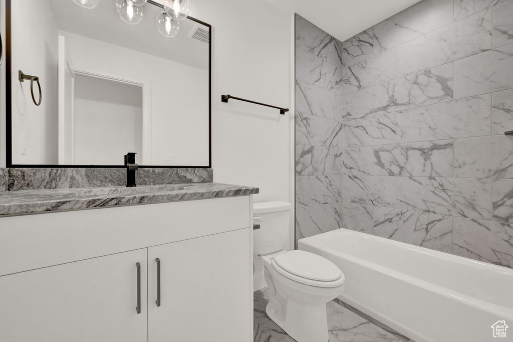 Full bathroom with tiled shower / bath, toilet, tile floors, and large vanity