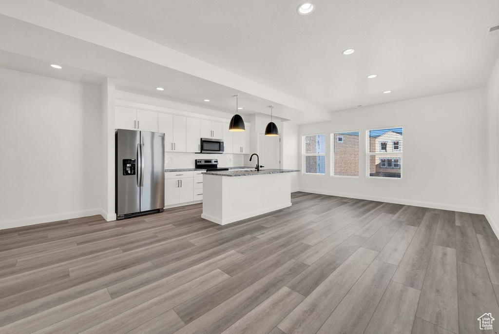 Kitchen featuring appliances with stainless steel finishes, light hardwood / wood-style flooring, white cabinets, a center island with sink, and light stone counters