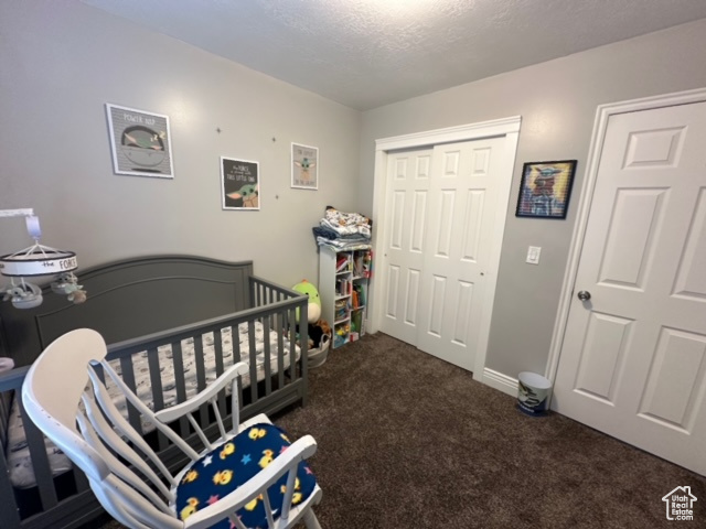 Carpeted bedroom with a nursery area, a textured ceiling, and a closet