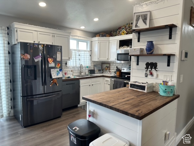 Kitchen featuring white cabinets, wooden counters, black appliances, tasteful backsplash, and hardwood / wood-style flooring