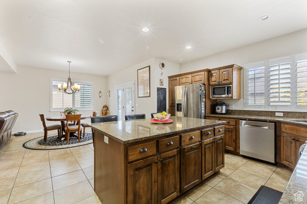 Kitchen featuring hanging light fixtures, an inviting chandelier, appliances with stainless steel finishes, light tile floors, and a kitchen island
