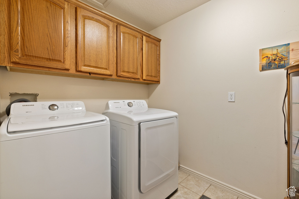Laundry room featuring light tile floors, cabinets, and washing machine and dryer