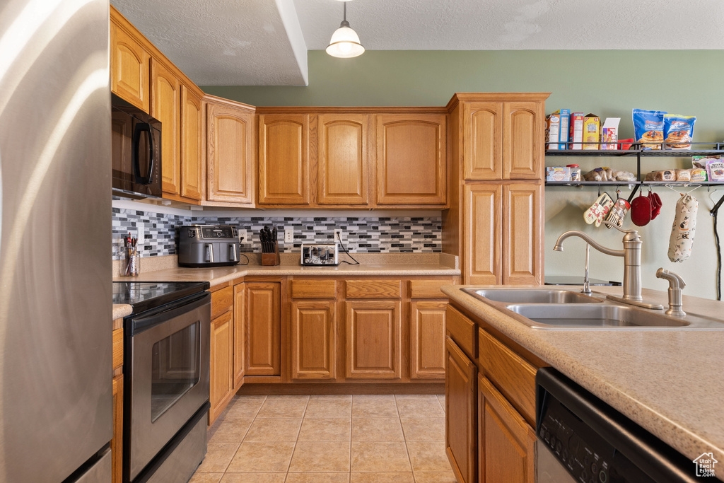 Kitchen featuring backsplash, light tile flooring, sink, stainless steel appliances, and pendant lighting