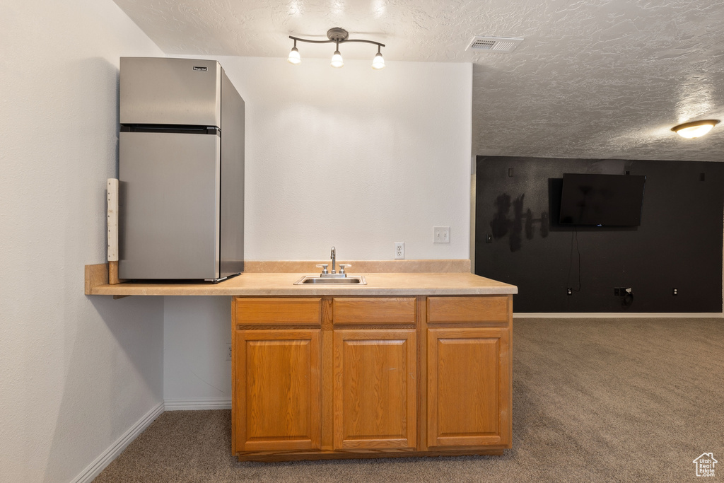 Kitchen with a textured ceiling, dark carpet, sink, stainless steel fridge, and track lighting