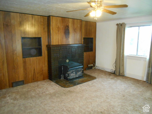 Living room with a brick fireplace, wooden walls, ceiling fan, and carpet