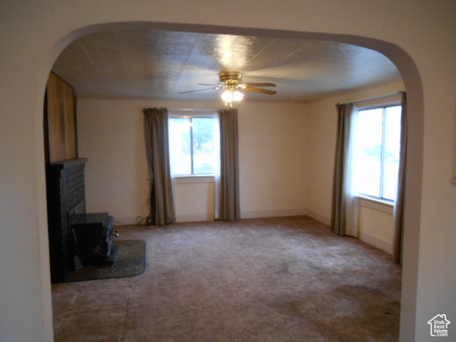 Unfurnished living room with light carpet, plenty of natural light, a brick fireplace, and ceiling fan