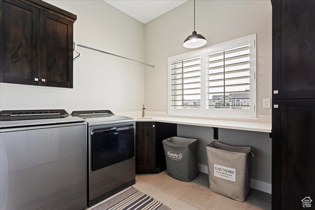 Clothes washing area with light tile flooring, sink, cabinets, and washer and clothes dryer