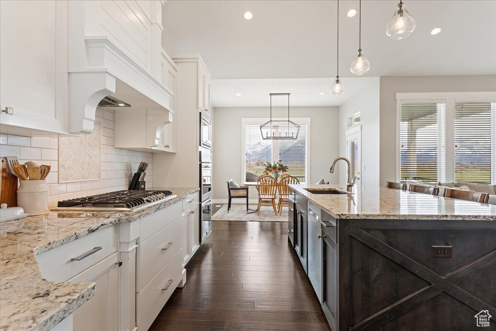 Kitchen featuring appliances with stainless steel finishes, decorative light fixtures, dark hardwood / wood-style flooring, and a kitchen island with sink