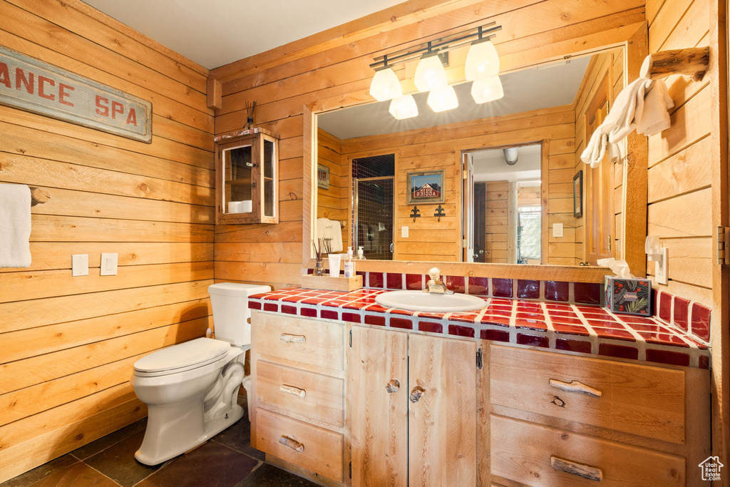 Bathroom with wooden walls, tile flooring, vanity with extensive cabinet space, and toilet