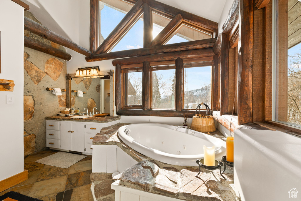 Bathroom featuring high vaulted ceiling, oversized vanity, a bathing tub, tile walls, and tile floors