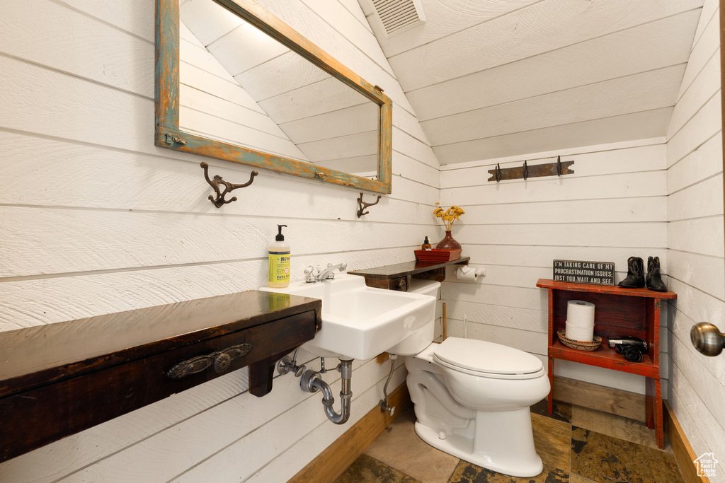 Bathroom featuring lofted ceiling, toilet, wood walls, and tile flooring