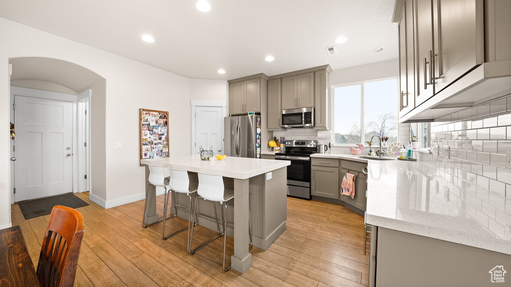 Kitchen with backsplash, light hardwood / wood-style floors, stainless steel appliances, and sink
