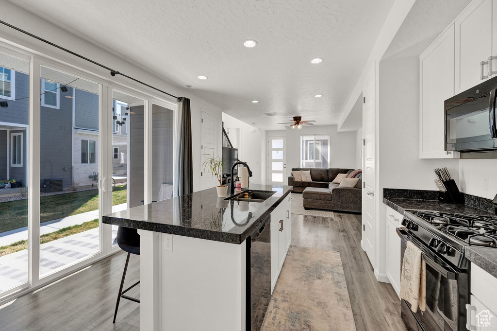 Kitchen featuring black appliances, ceiling fan, a kitchen bar, sink, and light hardwood / wood-style flooring