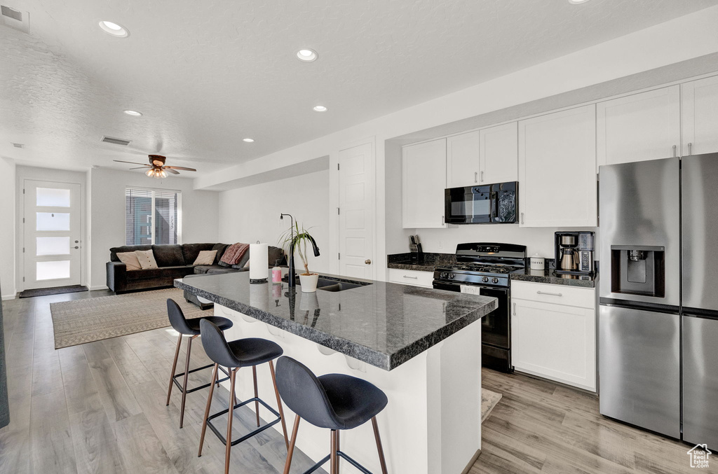 Kitchen featuring ceiling fan, sink, a breakfast bar, light hardwood / wood-style floors, and black appliances