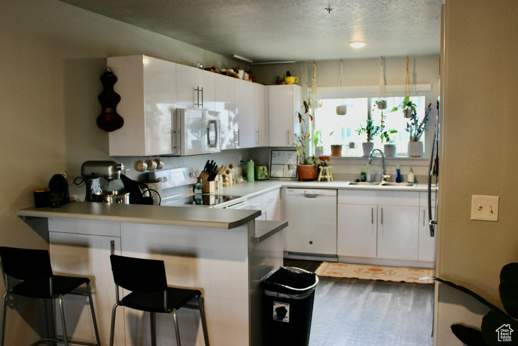 Kitchen with kitchen peninsula, white appliances, a kitchen breakfast bar, wood-type flooring, and white cabinetry