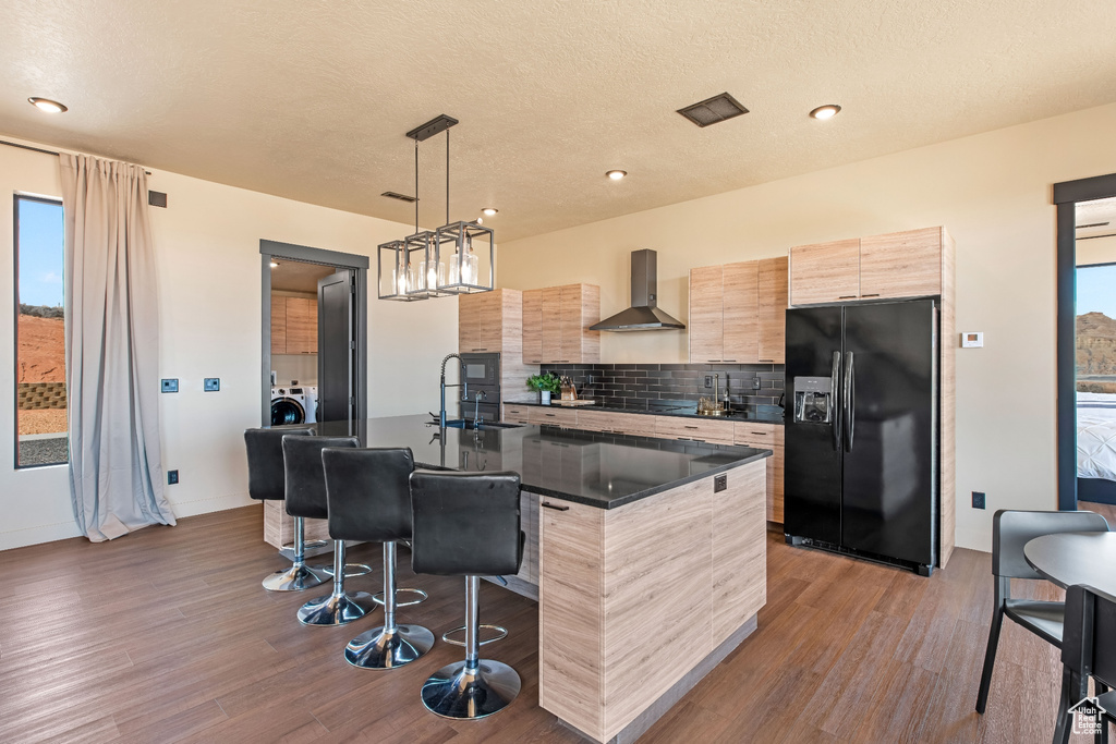 Kitchen featuring hanging light fixtures, black appliances, a breakfast bar, an island with sink, and wall chimney range hood
