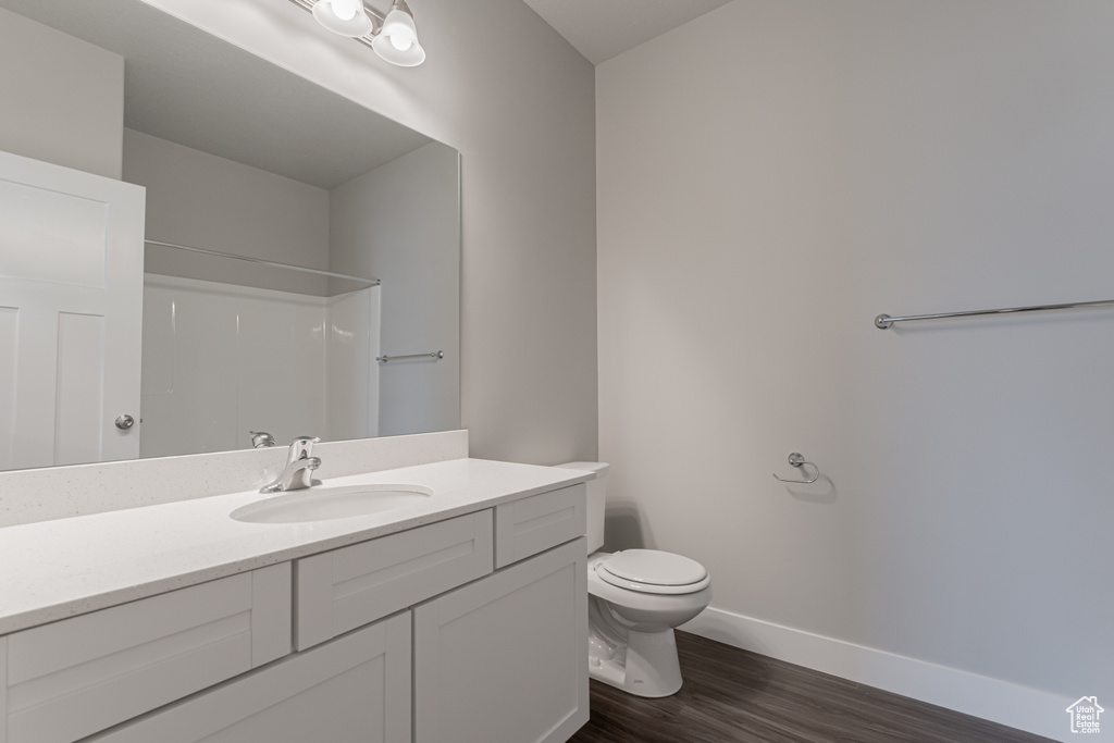 Bathroom with hardwood / wood-style floors, walk in shower, vanity, and toilet