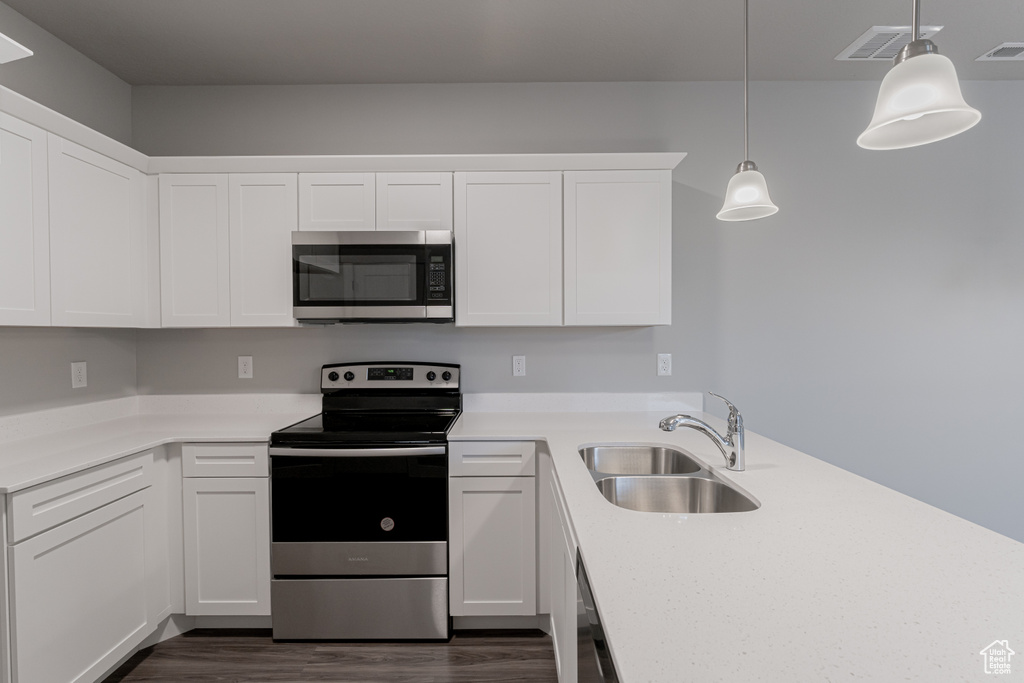 Kitchen featuring white cabinets, appliances with stainless steel finishes, decorative light fixtures, and sink