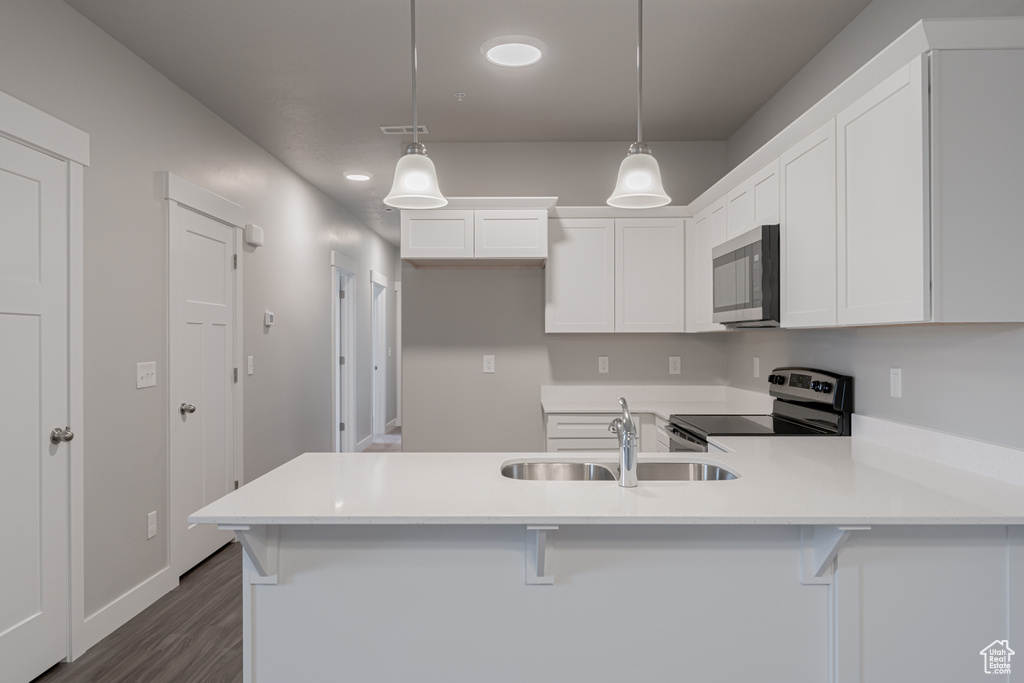 Kitchen featuring appliances with stainless steel finishes, white cabinets, a kitchen bar, decorative light fixtures, and sink