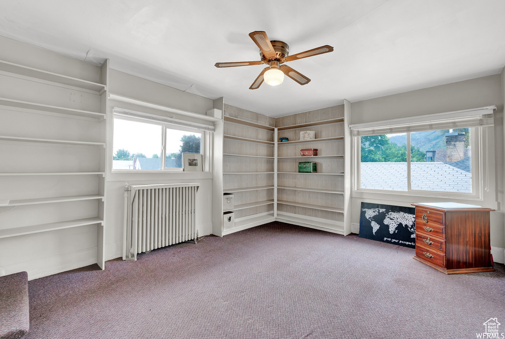 Carpeted empty room featuring ceiling fan and radiator heating unit