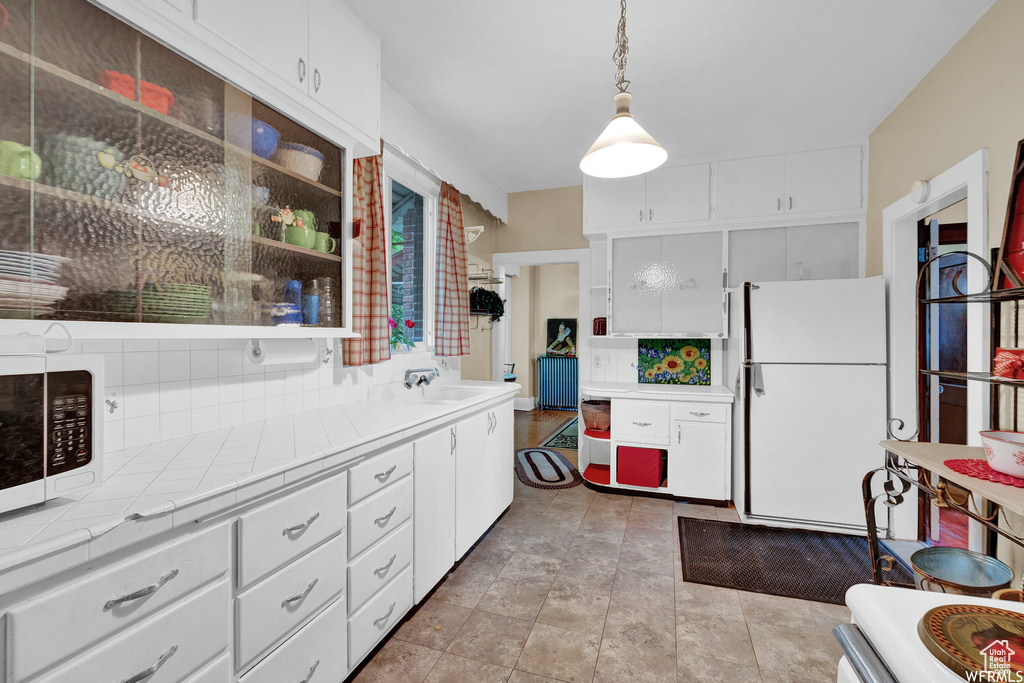 Kitchen with decorative light fixtures, white appliances, sink, white cabinets, and tile countertops