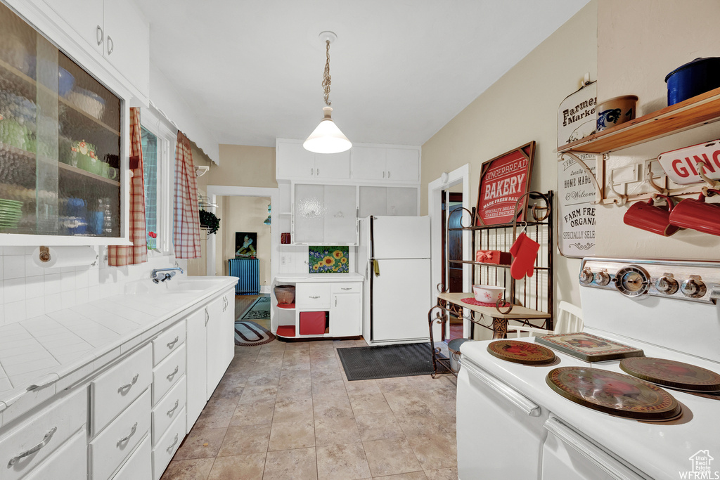 Kitchen featuring tile counters, light tile floors, white refrigerator, decorative light fixtures, and white cabinetry