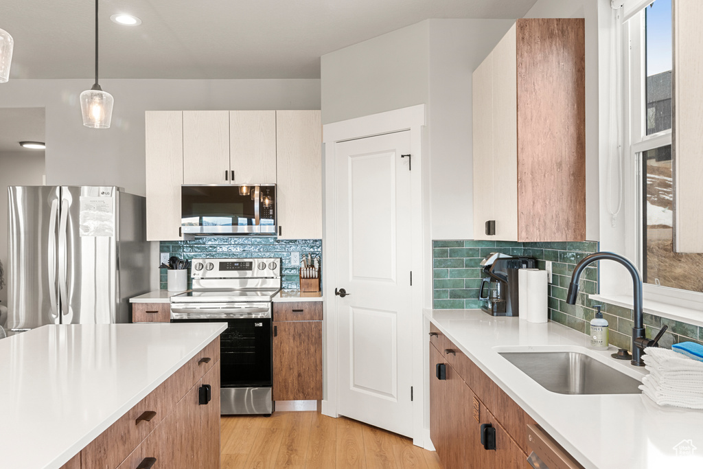 Kitchen featuring light hardwood / wood-style floors, decorative light fixtures, tasteful backsplash, appliances with stainless steel finishes, and sink